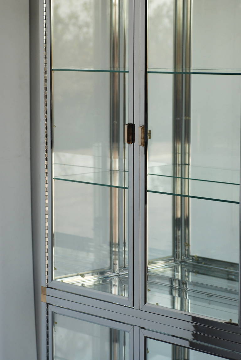 This gorgeous display case has glass on three sides and a mirrored back which reflects the light and the back of the objects inside beautifully.
The bottom shelf is smoked glass. The case is primarily finished in a beautiful chrome with brass at