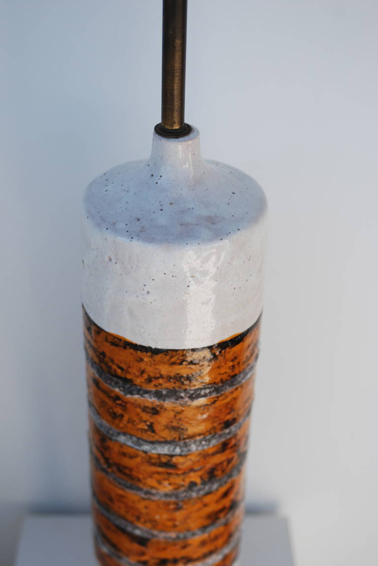 The color of the glaze on this cylindrical italian table lamp by Raymor is a beautiful burnt orange over plaster white with some charcoal mixed in.
The lamp is signed at the bottom.