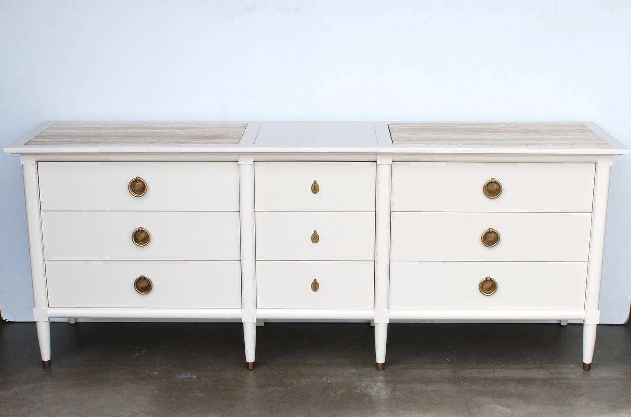 This crisp chest retains its original antique brass hardware. There are two removable Italian travertine marble tops inlaid flush with the top. The piece has been freshly lacquered in a pleasing bone white color. There are nine drawers in the buffet