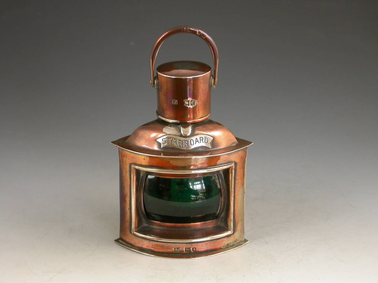 A Victorian novelty silver Cigar Table Lighter made in the form of a Ship's Starboard Lantern, with a green glass lens and hinged cover opening to reveal the removable cylindrical lighter reservoir. 

By Samuel Jacob, London, 1898