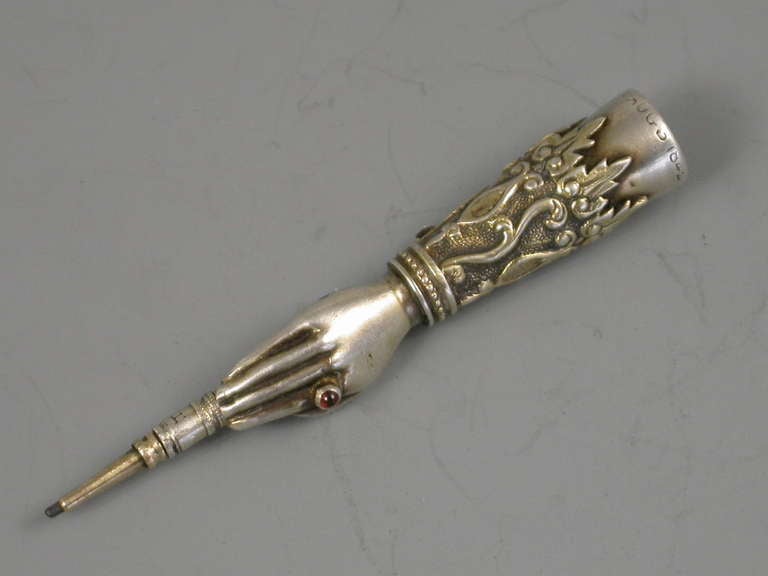 A very rare and early Victorian novelty silver Sliding Pencil, modelled in the form of a hand with red garnet ring on the index finger, applied and gilded decoration to the cuff. The terminal set with an amethyst coloured seal stone.

Stamped S