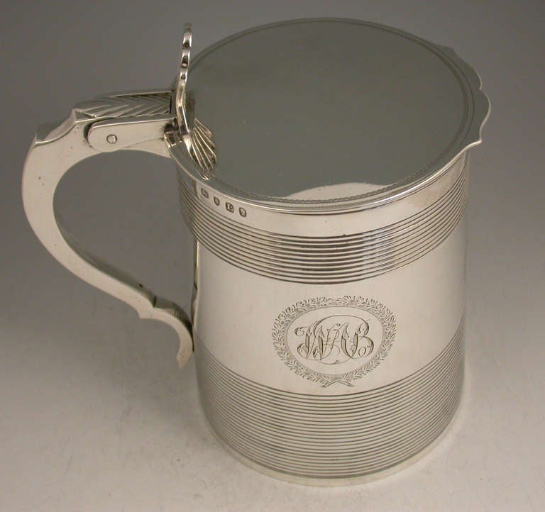 A fine quality George III flat lidded Tankard with straight tapering sides and reeded decoration, pierced fan shaped thumb piece and leaf capped scroll handle. The body engraved with three circular cartouches surrounded by wreaths, one engraved with