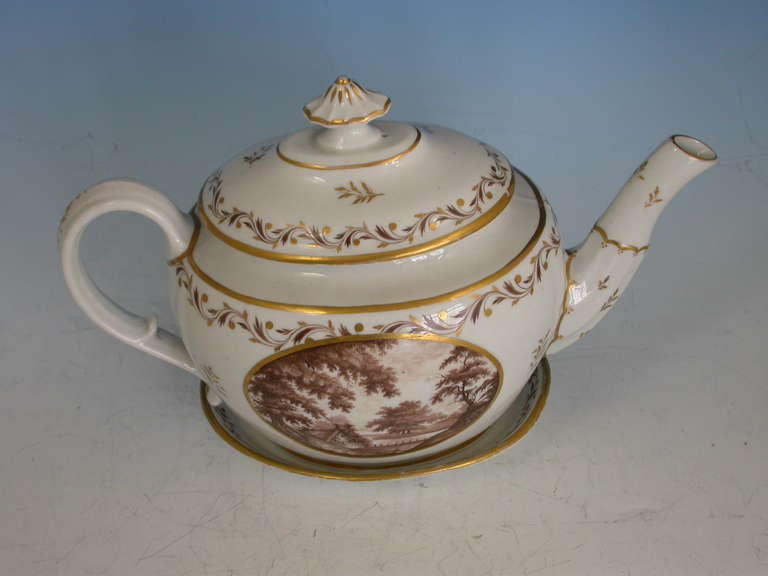 A very rare John Rose Coalport Teapot, Cover and Stand, of oval form with ear shaped handle and faceted spout, the cover with mushroom finial. Painted within the gilt enriched oval reserve with a landscape scene in sepia depicting a meandering river