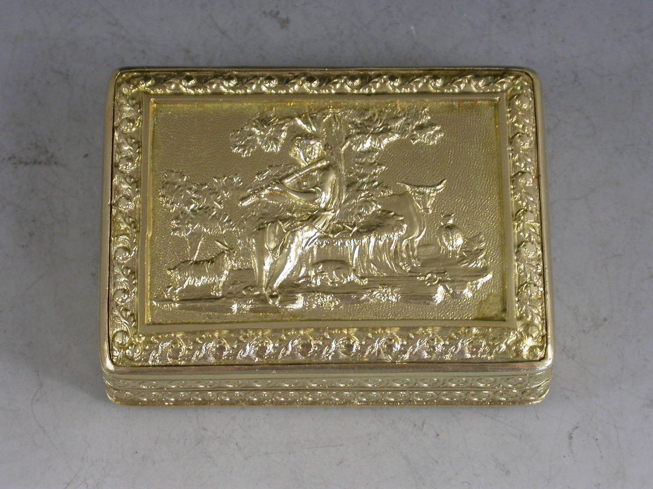An exceptional George III silver gilt Vinaigrette of very large size and rectangular form with raised foliate borders, the plain base with engraved foliate border, the lid with a raised chased scene on a matt background depicting a Shepherd Boy