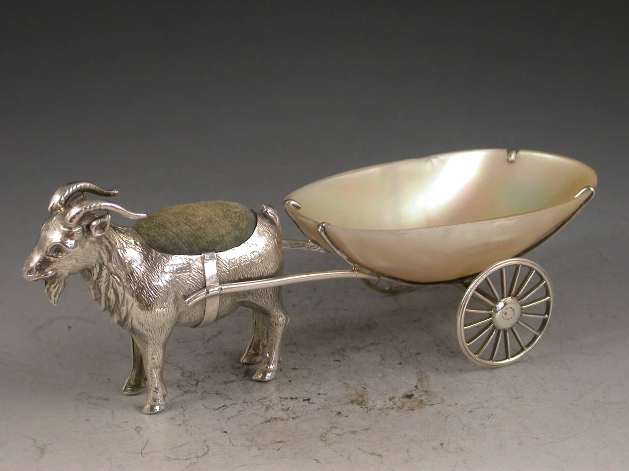 A rare Edwardian novelty silver Pin cushion made in the form of a Goat pulling a mother of pearl cart with two revolving silver wheels. 

By Adie & Lovekin, Birmingham, 1910
