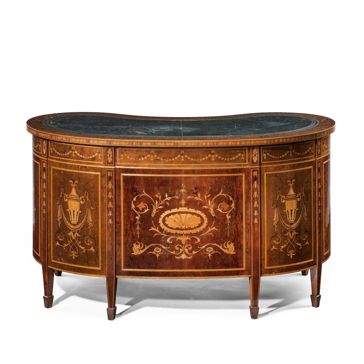 A fine freestanding kidney shaped mahogany desk by Druce & Co, decorated overall in satinwood marquetry and crossbanding with an acanthus wave scroll, harebells, classical urns and a stylized central shell motif. With a plate inscribed Druce & Co,