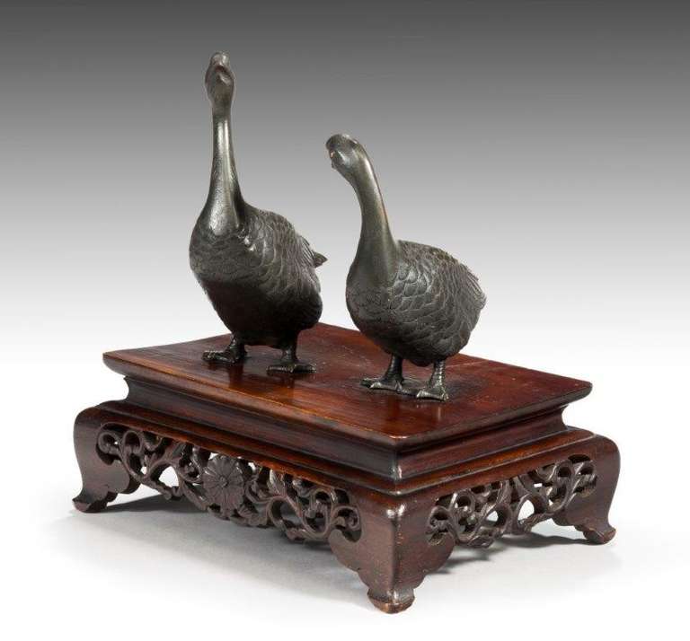 A pair of Meiji bronze geese stood upon a hard wood stand.