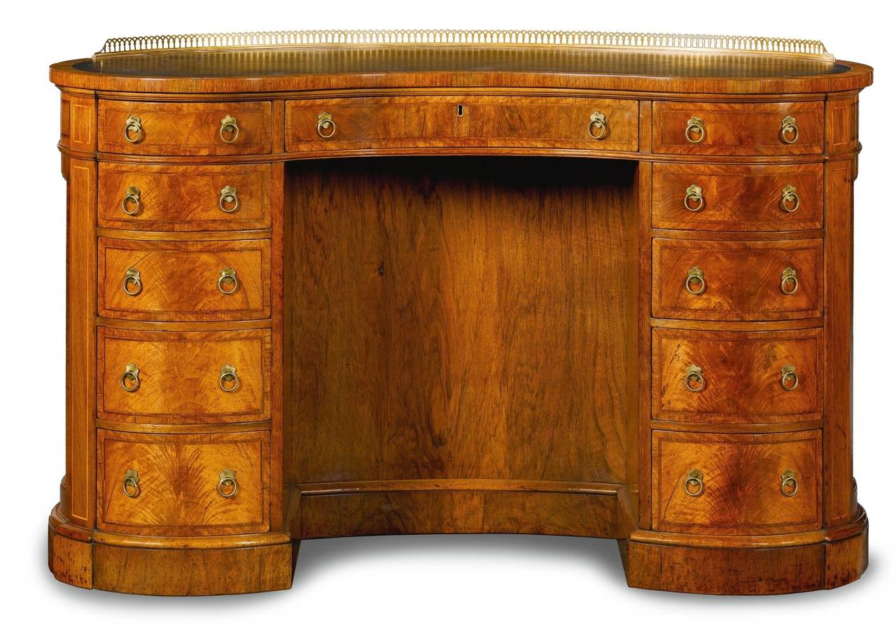 VICTORIAN WALNUT AND FEATHER BANDED KIDNEY SHAPED KNEEHOLE DESK with a replaced tooled leather inset top with a pierced brass gallery above three frieze drawers and eight pedestal drawers, with open shelves to the back, on a plinth.