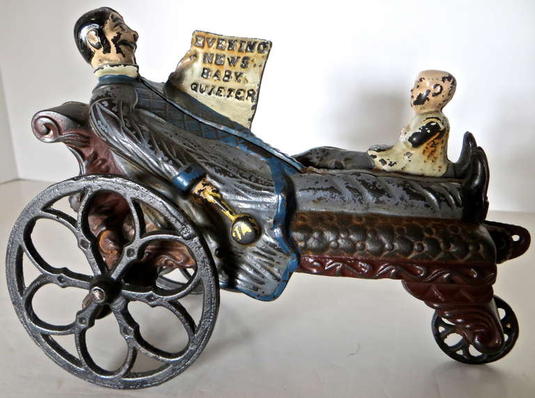 Cast iron toy becomes articulated when pulled along the ground or pushed along a table top. The father while reclining on the couch and with the baby resting on his leg, keeps the child quiet by lifting his left leg up and down while reading his