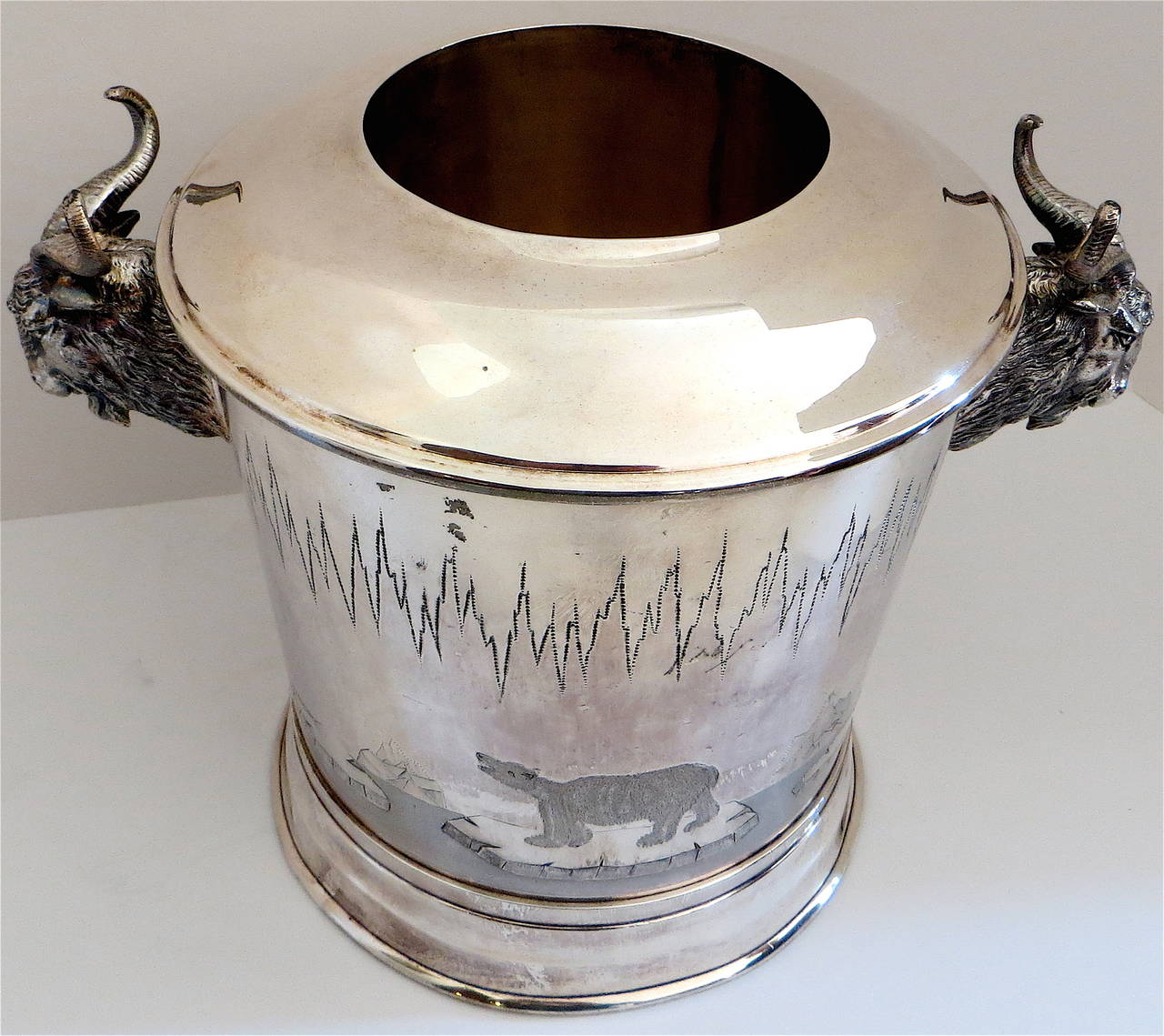 An unusual ice bucket with a western theme, depicting ram's heads on opposite sides for carrying; additionally decorated on both sides with engravings of a polar bear on ice in an Arctic setting. Removable middle cylinder accommodated the bottle of