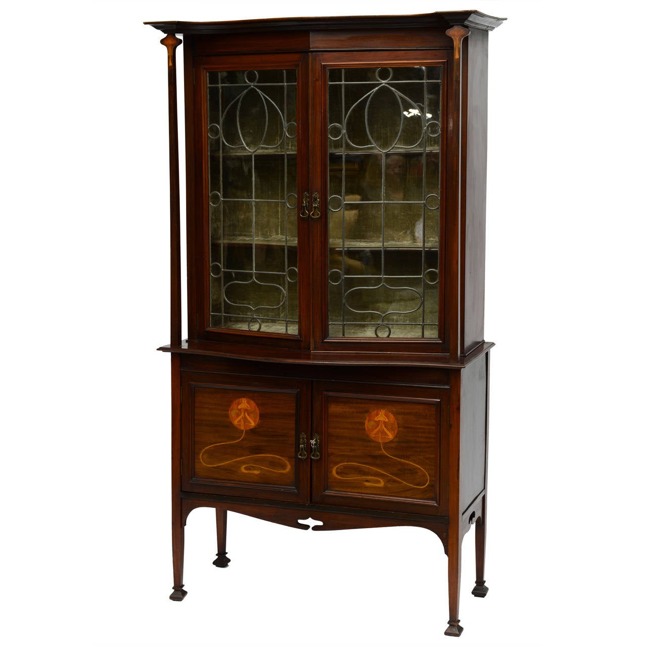 A beautiful iconic Galle/Majorelle style Art Nouveau mahogany cabinet with gracefully tapered columns terminating in stylized marquetry flora capitals under a stepped overhang pediment. The columns flank the pair of leaded clear glass doors