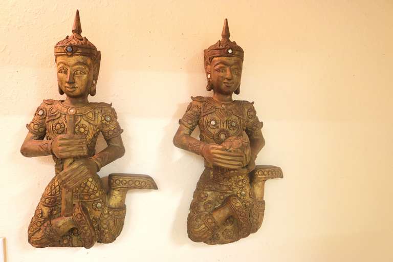 19th c. pair of elegant Large Siamese gilt carved teakwood figures one a musician holding a flute and one dancer holding a basket of flowers love and peace offering. each in a seated position and wearing reflective gem bordered costumes beneath a