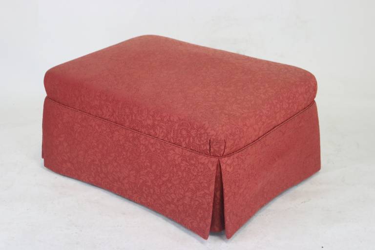 Lovely ottoman upholstered in a medium rosy red tone on tone Scalamandre Cotton and Linen Floral Brocade, upholstered with lined dressmaker's skirt, fabric covered recessed legs. Nicely detailed with the tight top pleated tuck corners and welt trim,