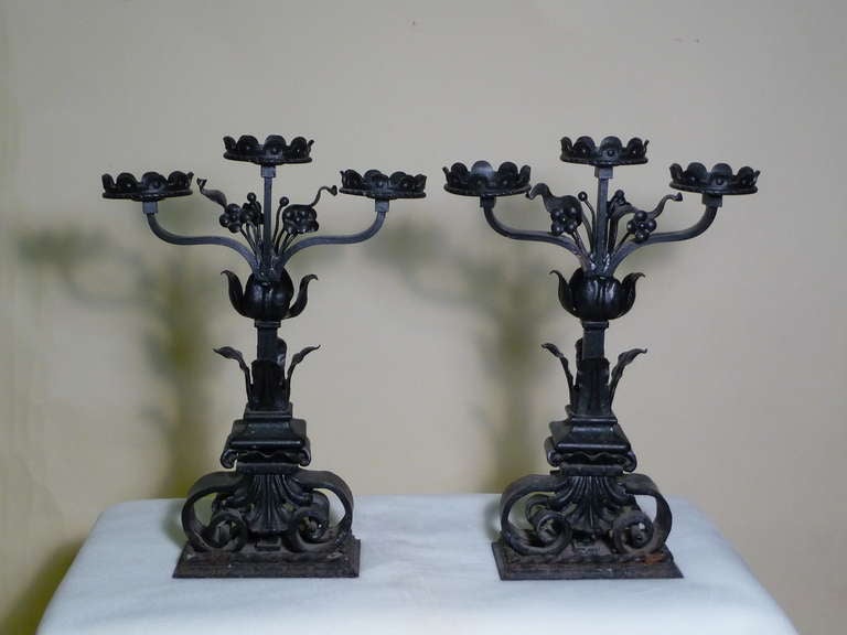Masterful Finely Detailed large pair of continental black iron Candelabras—three-arm for large candles--adorned with flowers and leaves with scrolling legs on a plinth base- in a Gothic Renaissance style--hand forged by a masterful artisan craftsman