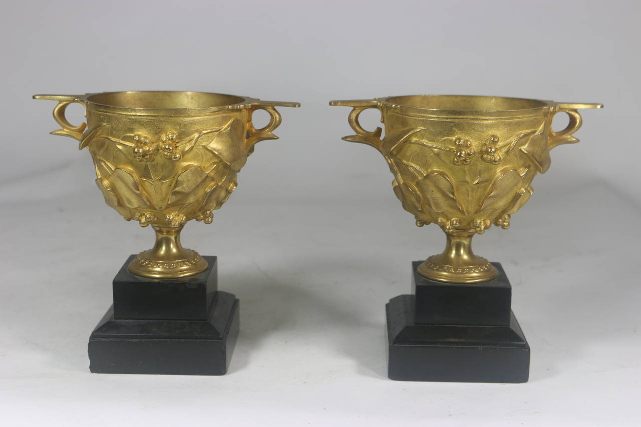 19th century magnificent rare pair of core bronze exuberant Roman style decorated urns with highly raised finely detailed swirling vine leaves and berries on black marble bases. This pattern is based on a Roman design discovered in the excavation of