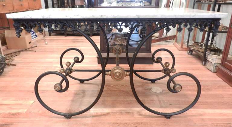 Antique French pastry or butcher's table melds brass and steel, with its classic scrolling base, decorative edging and a white Carrera marble top.  These beautiful tables are typically 19th century and feature a cast and wrought iron base with a