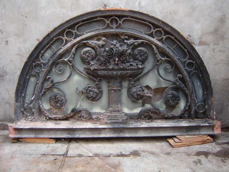 This wrought iron transom window depicts an urn filled with roses. Incredible ironwork. It originally graced a building's entryway in Argentina.  The glass has since been broken which can be easily replaced.  This item can be seen at our National