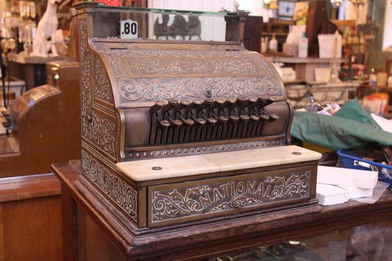Bronze cash register by National.  Highly decorative detailing with a milk glass shelf. The company began as the National Manufacturing Company of Dayton, Ohio, which was established to manufacture and sell the first mechanical cash register,