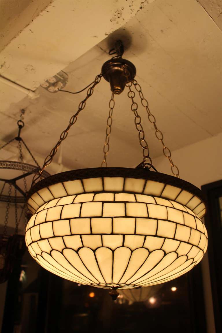 An Edwardian style curved and leaded glass inverted dome fixture. Shown here with a dark aged brass fixture with four hanging chains.  The glass has a slight bronze tinge to it.  This item can be seen at our Chelsea location.