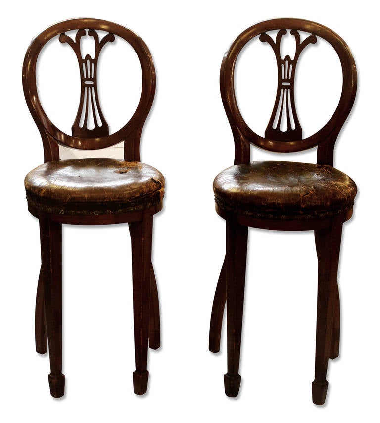 This is a pair of English chairs or stools with heavily worn leather seats with rivets. Simple wood legs and wooden back with cutouts. These can be seen at our 5 East 16th St. store on Union Square.