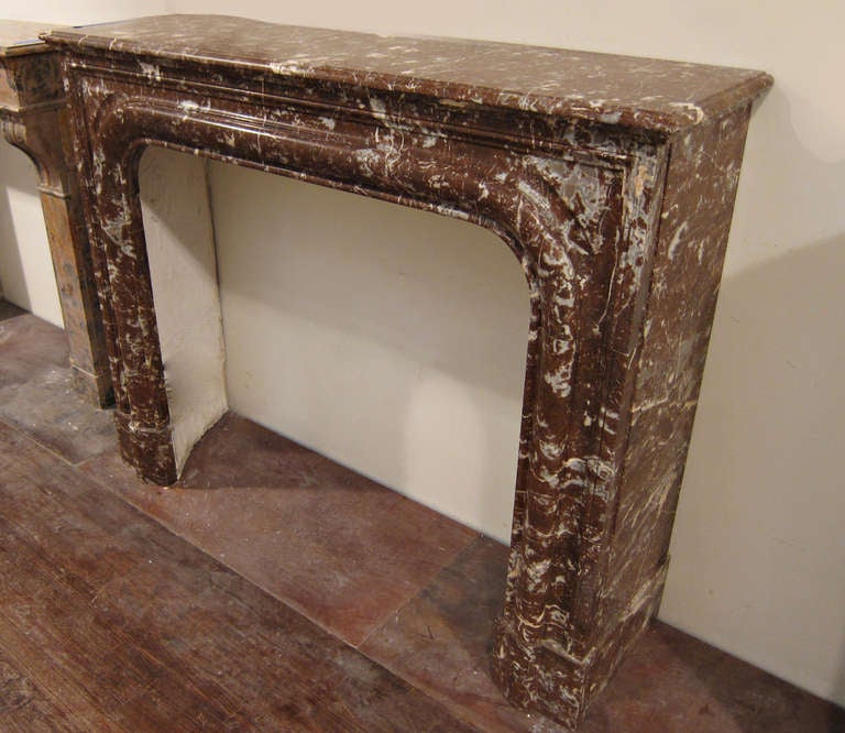 This French Rouge Royale marble mantel has a graduated arched frieze with very simple lines. There is a crack down the middle of the shelf which has been carefully repaired. It's difficult to see due to the veining of the marble. This is one of