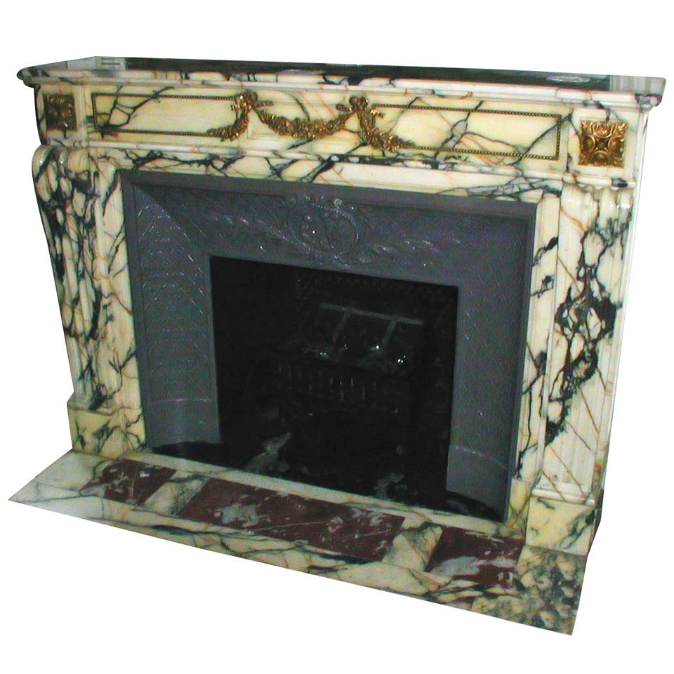 This authentic marble mantel, dating back to the early 1900s, was salvaged from the historic Plaza Hotel in NYC and acquired by Olde Good Things in 2005. The marble features a distinctive blend of gold and dark veins, complemented by ornate bronze