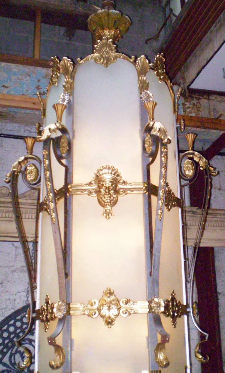 This is a very tall Art Deco hanging light or chandelier that was salvaged from a theater in Brooklyn, NY. It has glass panels in a steel and bronze frame, with faces around the outside, and botanical motif. The glass panels are about an inch thick.