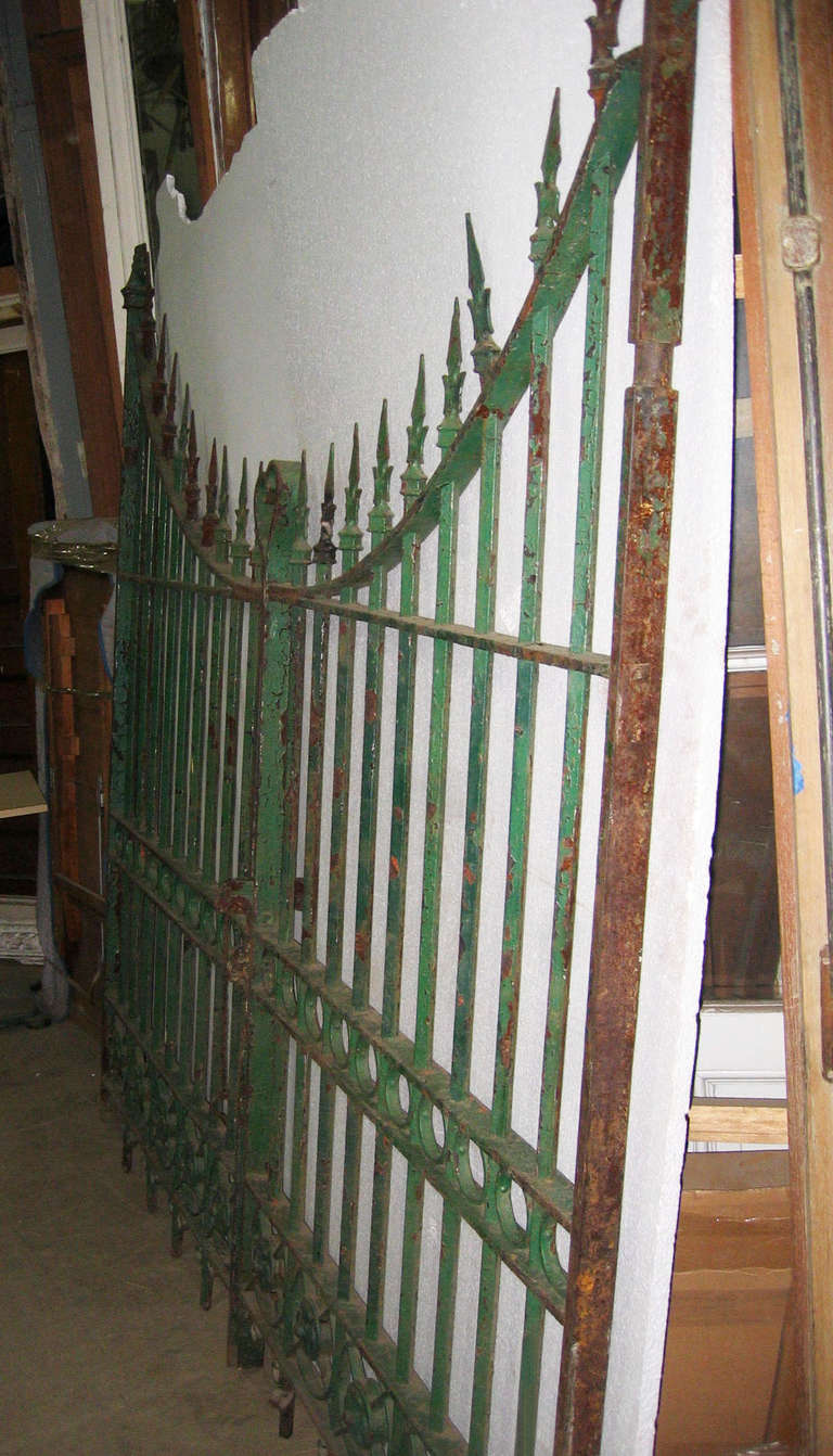 Arched with cast iron quatrefoils on bottom and topped with bold French arrow finials. These are a heavy gauge good quality iron with distressed green paint. Just over 8 ft wide opening. Sold as a pair.