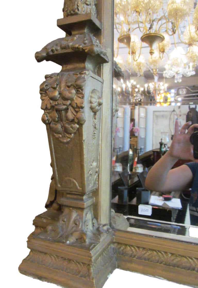 This is a large 19th century gilt overmantel mirror with an ornate frame. The mirror has a wide bevel and is in good condition. The detailed carvings add a beautiful Victorian accent to this magnificent piece. This item can be seen at our 124 West