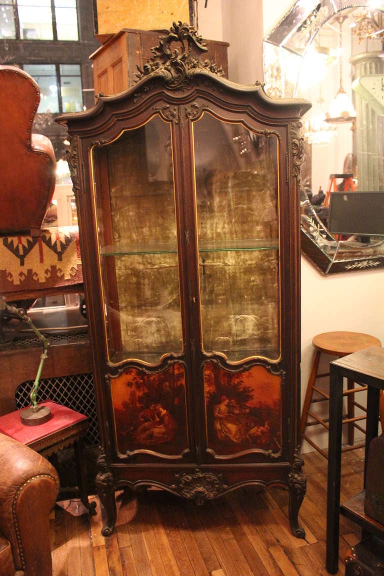 Louis XV style vitrine with hand-carved molding throughout, painted motif door panels, velvet lined backing and two adjustable glass shelves. Glass displayed on the front and both sides.