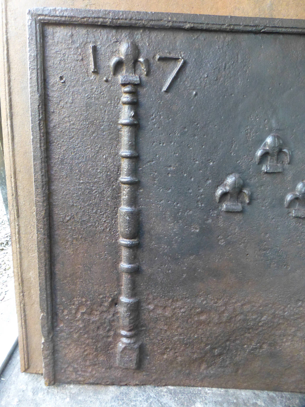Säulen mit Fleurs de Lys aus dem 18. Jahrhundert, Das Herstellungsdatum 1791 ist ebenfalls in die Rückwand eingegossen. Die Feuerrückwand ist aus Gusseisen und hat eine natürliche braune Patina. Auf Anfrage kann er auch in schwarz/zinnfarbener