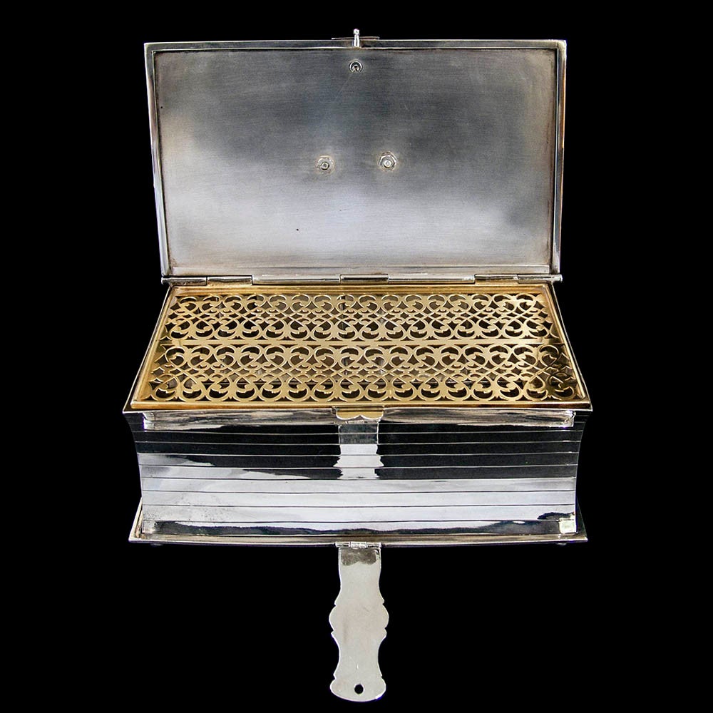 A very decorative silver plated biscuit box in the form of a book.The lid decorated with engraved pattern and surmounted by a a handle in the form of a ribbon bow. Decorated in the style of hand-tooled leather. The lid kept closed by a metal strap.