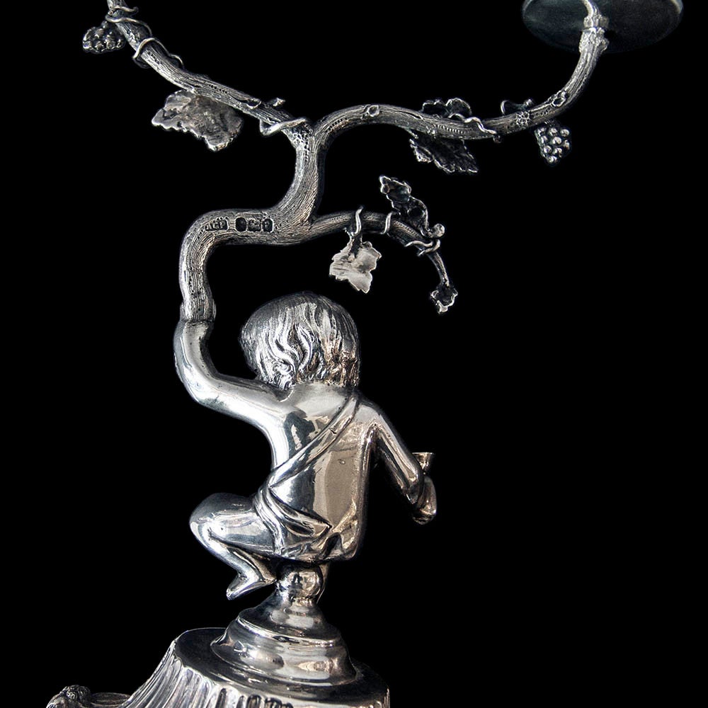 A pair of bacchanalean figural candelabra.Each seated figure holding a wine goblet in the right hand and a branch with trailing grape vine surmpunted by 2 candle holders.