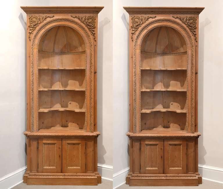 Pair of early 19th century, French, corner cabinets. Composed of pinewood, these exquisitely crafted, sturdy cabinets feature unusually curved, stationary shelving. Regal crown molding is accentuated by arched panels that feature elaborately carved