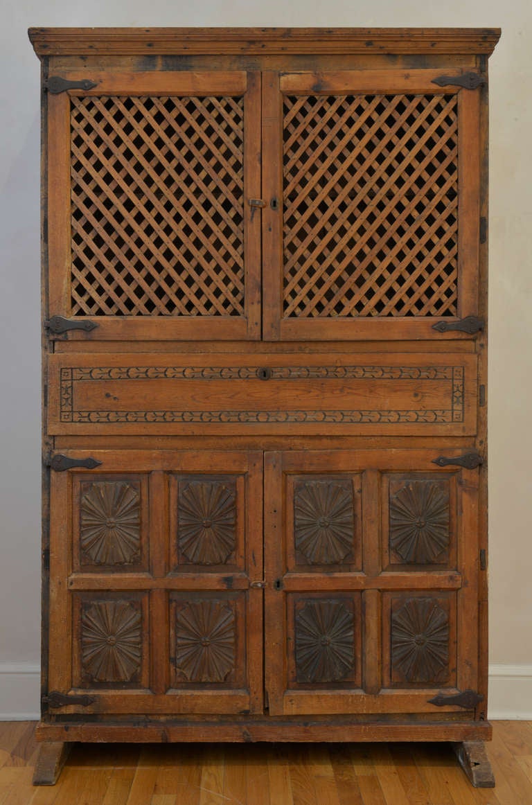 This tall 18th Century Mexican fresquera of northern indigenous white pine features cornice crown molding, ventilated lattice top doors and two lower doors attached with iron strap hinges. The piece has exquisitely carved recessed rosette panels on