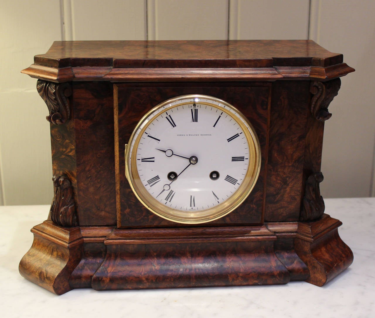 An early-Victorian mantel with stunning burr walnut veneers. The rectangular case has step front moldings and canted corners with carved details. It has a white enamel dial signed by the original retailer/maker James and Walter Marshall of Edinburgh