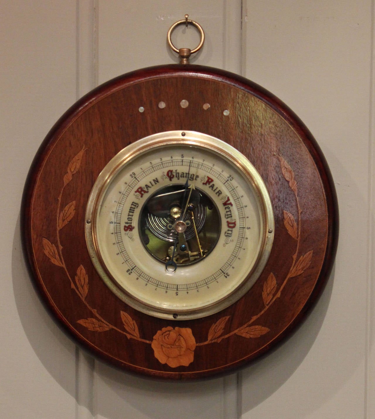 A small circular barometer, having a beechwood and walnut case, inlaid with floral satinwood decoration. It has a visible aneroid movement and a bevel edge glass.

Diameter	15.00cm