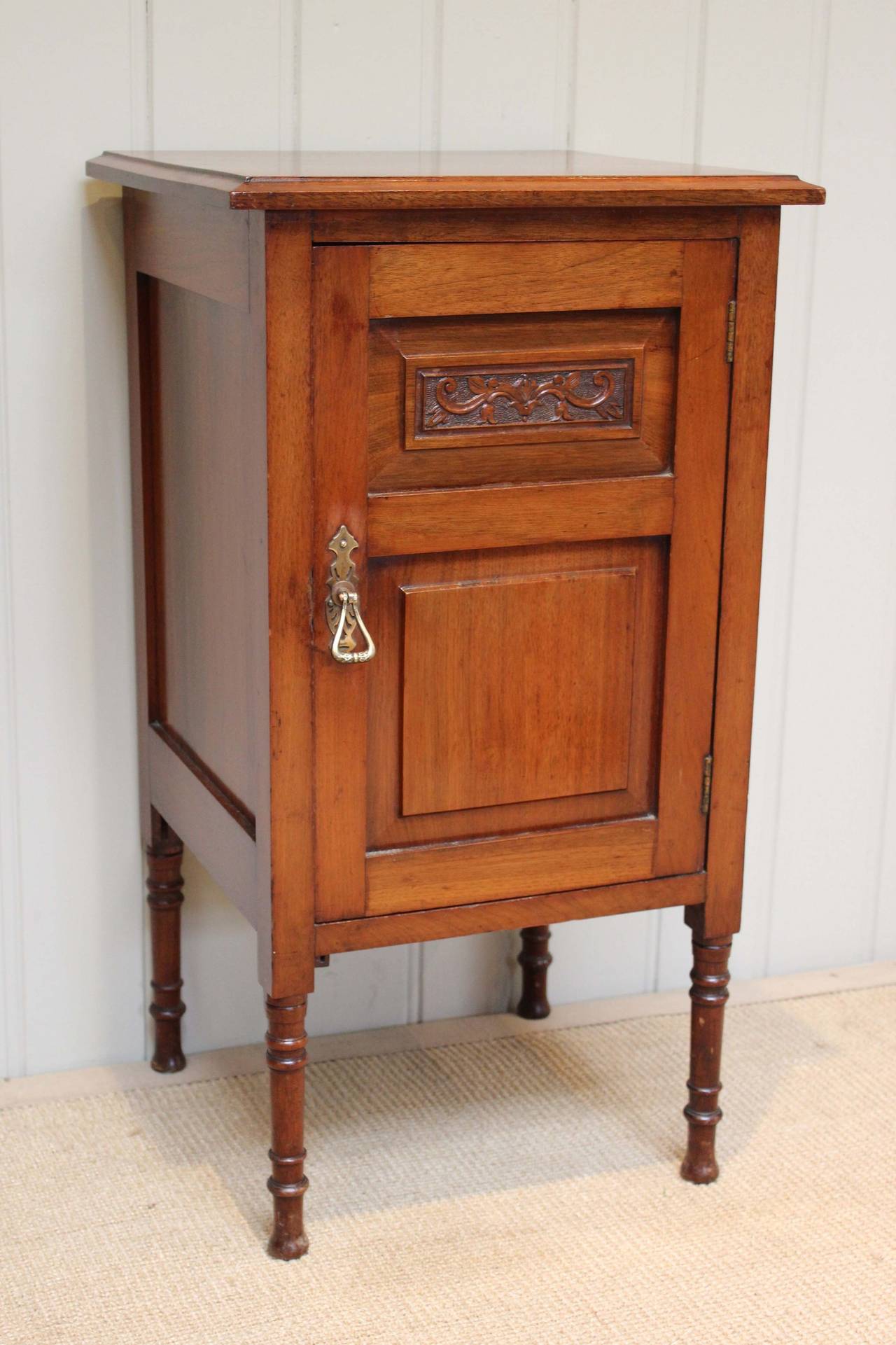 Edwardian walnut bedside cabinet having a single panelled door having a carved detail opening to reveal an interior shelf raised on turned wooden legs.