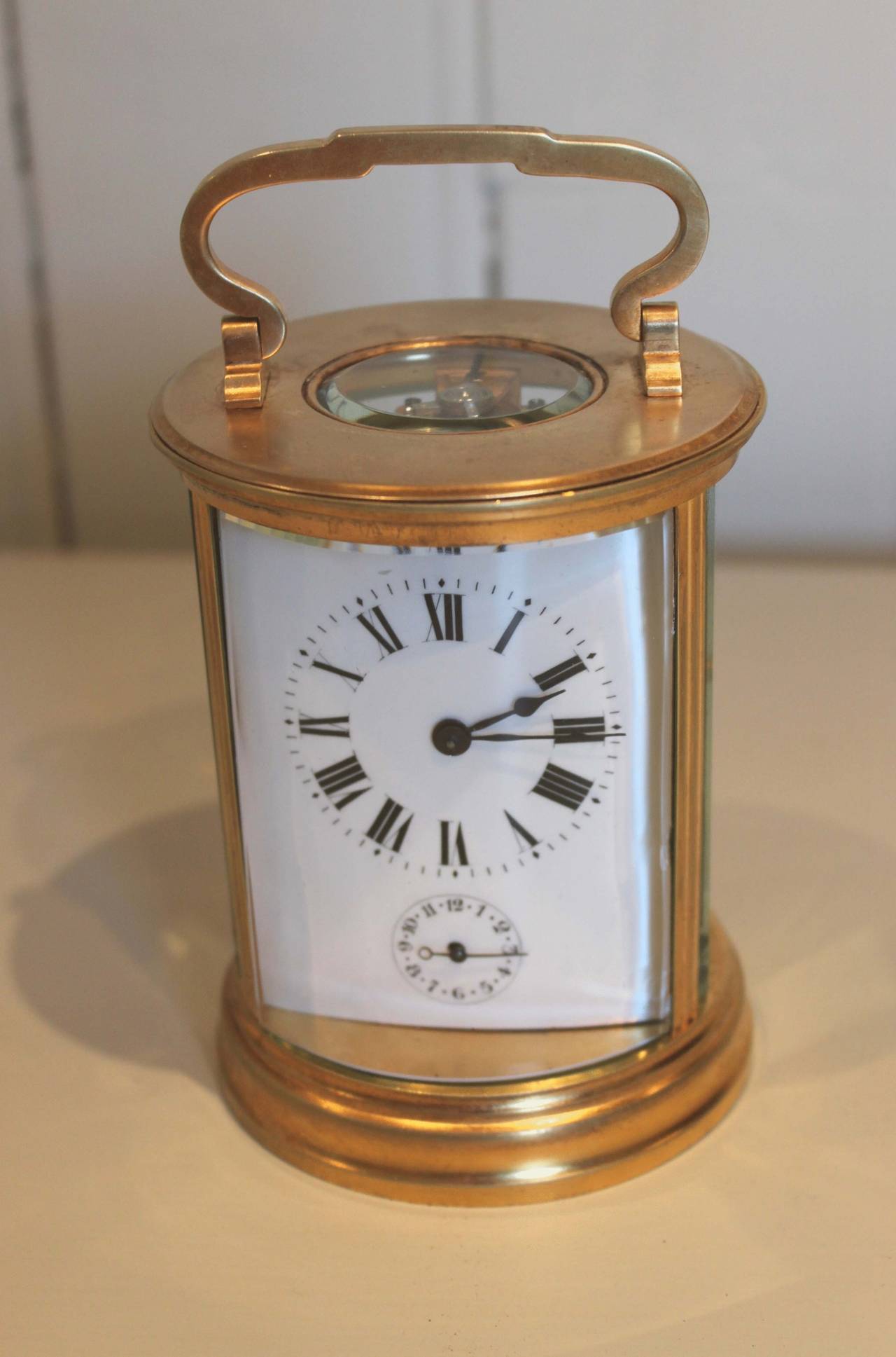 An unusual Timepiece carriage clock with alarm mechanism in a cicular case retaining its original gilding. It has a bow glass front and back and a top circular window. The curved enamel dial has Roman numerals and a subsidiary alarm dial. The 8 day