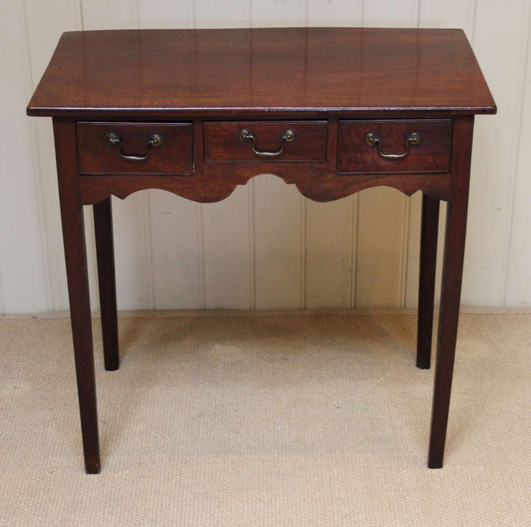 A delightful, country made solid mahogany lowboy. It has a solid top, with an arrangement of a central drawer flanked by two side drawers with a shaped apron, on straight supports. The drawers have their original brass swan neck handles.