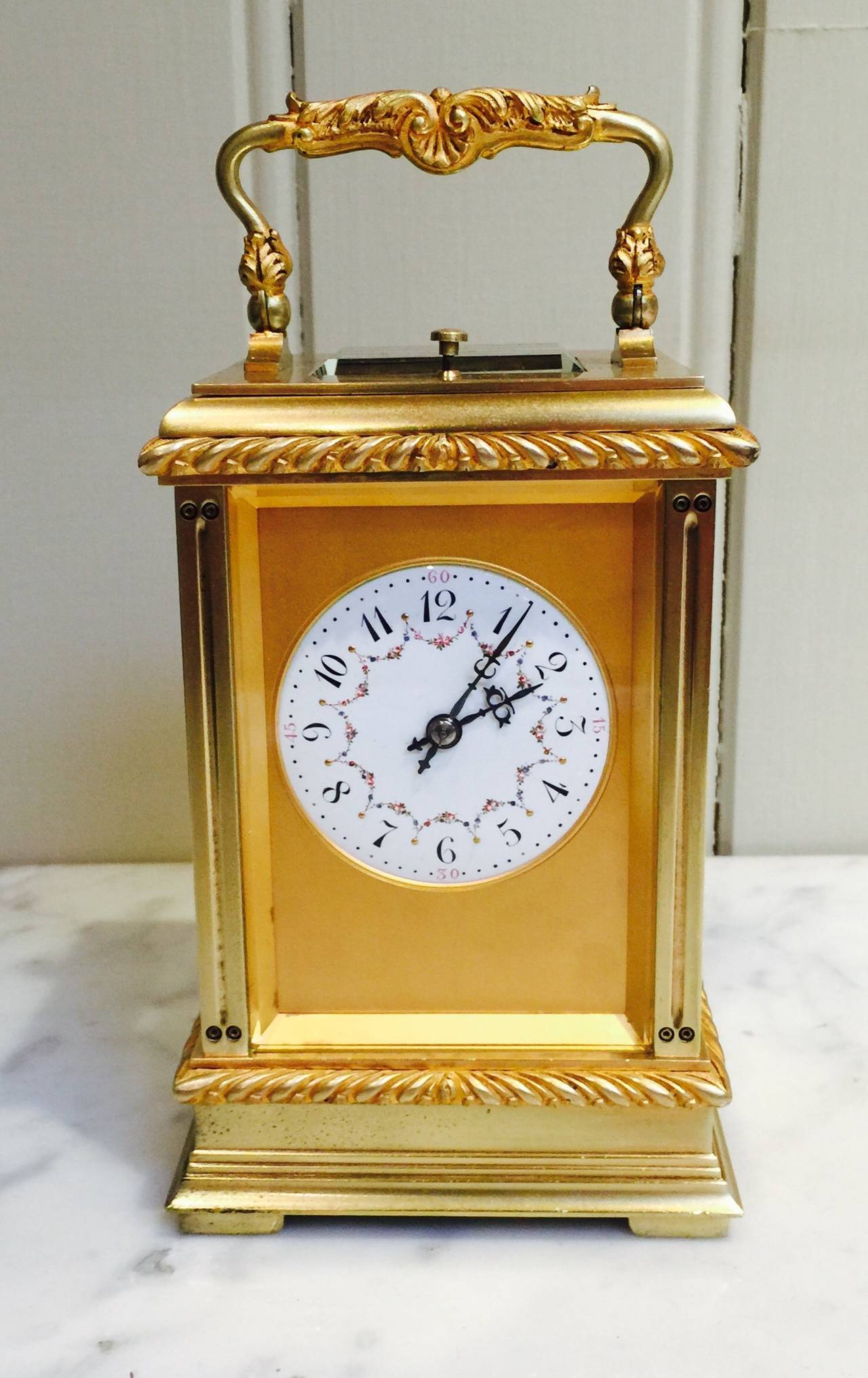 Un orologio da carrozza decorativo in ottone risalente al periodo tardo vittoriano/edoardiano. Ha una cassa goffrata con una maniglia decorata per il trasporto, una mascherina dorata per il quadrante e un quadrante decorato a mano con smalto