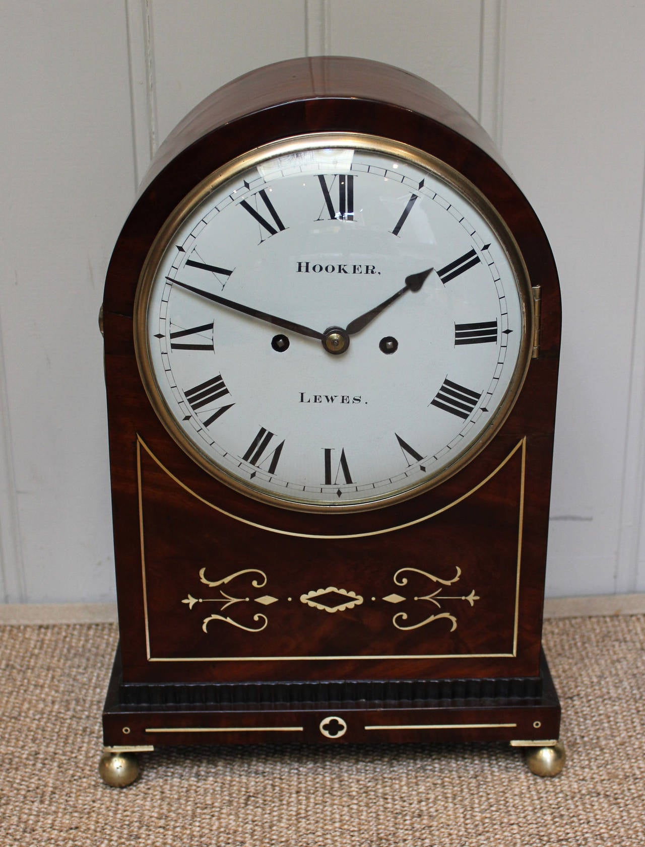 An early 19th Century Regency mahogany bracket clock, with brass inlay. The arch top case has a figure mahogany front panel with inlaid brass, the sides have brass loop handles and fish scale fret sides with red silk set behind and adjustable brass
