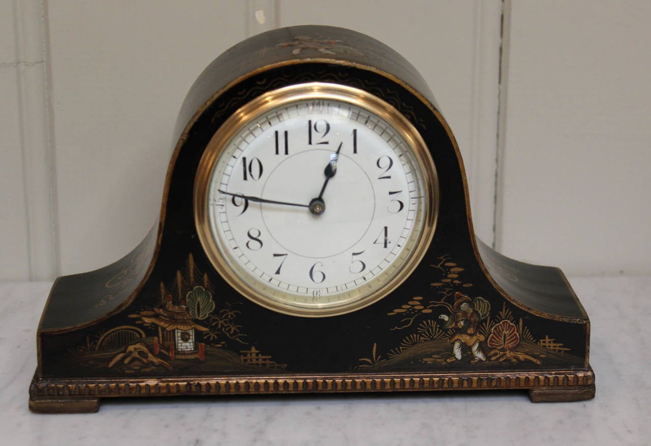 A 1920's black ground mantel clock with oriental style chinoiserie decoration. It has a swept arch case in the shape of a Napoleon hat, with a beaded molded edge. The enamel dial has a polished edge convex glass and an 8 day French movement with a