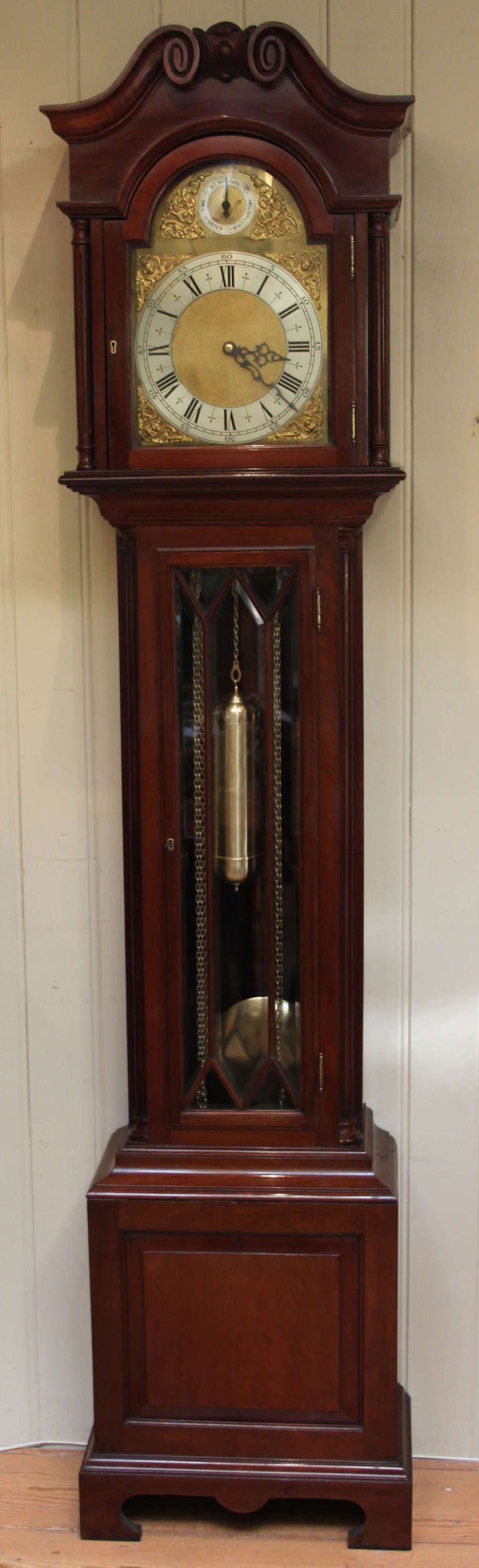 A good quality Edwardian solid mahogany musical longcase clock. The case is in an 18th Century style, having a carved swan neck pediment with a central cartouche, reeded side columns, and a break arch hood with side windows. The long door has glazed
