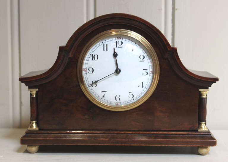An arch top case mantel clock, having a burr walnut case with inset side columns with brass capitals and brass ball feet. It has an enamel dial and a French 8 day timepiece movement with cylinder platform. 

England and France