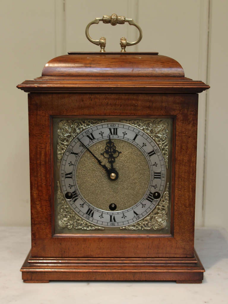 A walnut Cased Bracket Clock in The late C17th Century style. It has a bell top case with a brass carrying handle, and side windows. The square dial has an engraved chapter ring and corner spandrels. It has an 8 day Westminster 1/4 Chime platform