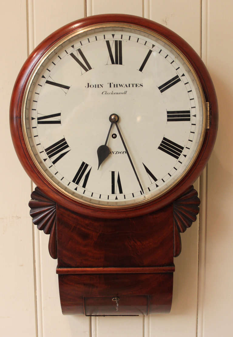 A nicely proportioned wall clock, that has a convex curved base box. The outer mahogany rim has a cast brass bezel, and a the base box has curl figured veneers,and a base door for the pendulum regulation. It has a white enamel dial signed by the