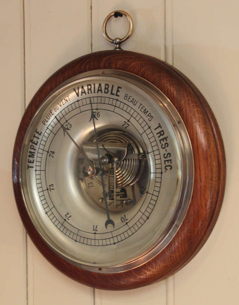 An unusually Large circular oak barometer. It has a turned wooden surround with a visible nickel plated aneroid movement. It has a very thick bevel glass with a reverse painted barometric scale. 