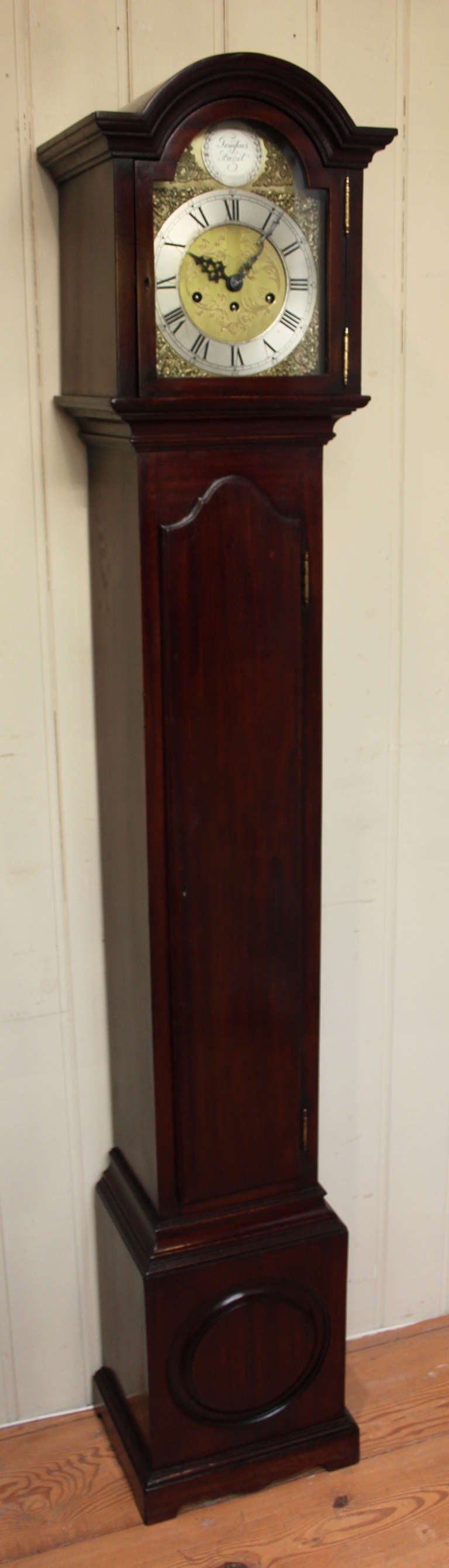 An attractive and well proportioned grandmother clock made in the late 18th Century style. It has a break arch top, a long door and a roundel molding in the base. It has a brass dial with a silvered chapter ring and a Tempus Fugit disc within the