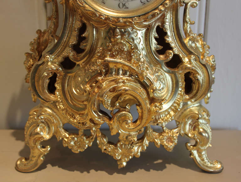A French mid 19th Century gilt brass mantel clock in the Louis XV style. It has a Rococo case embossed with acanthus leaves and scrolls. It has a convex glass and a cream enamel dial with tasteful blue numbering. The 8 day movement strikes the hours